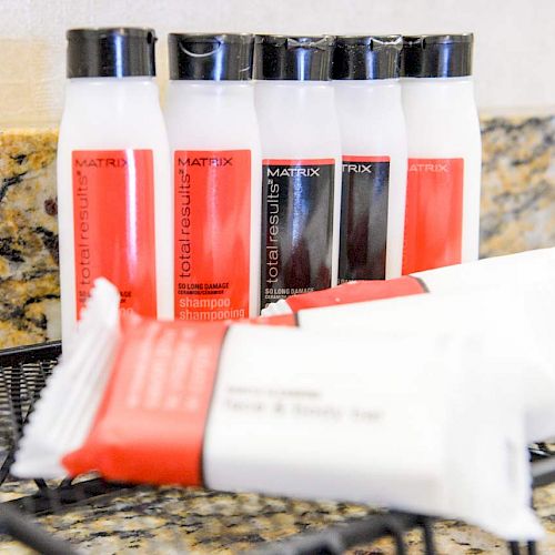 The image shows toiletries including bottles of shampoo and conditioner, and packaged soap bars on a shelf in a bathroom setting.