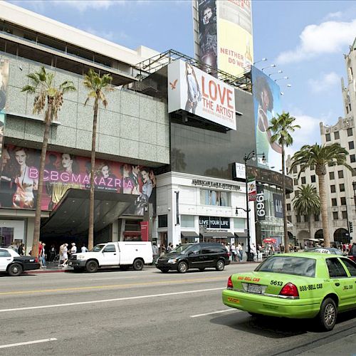 City street scene with cars, palm trees, and various advertisements on a building. One prominent ad reads 