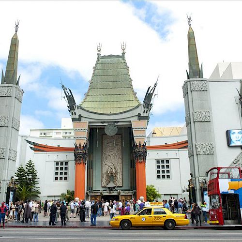 The image shows the entrance of a grand building with a green pagoda-style roof, crowds of people, a yellow taxi, and a double-decker bus.