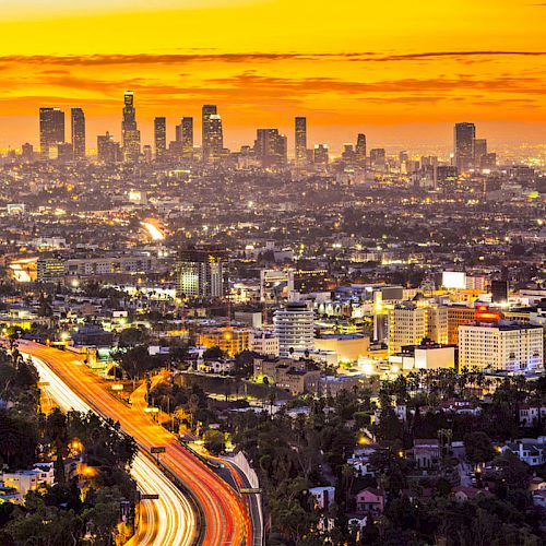 The image shows a cityscape at sunset with skyscrapers in the distance and illuminated roads, creating a vibrant and dynamic urban scene.