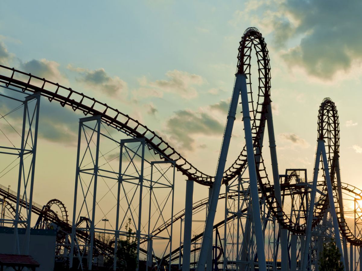 The image shows a roller coaster with a looping track against a sunset sky, with steel structures and a few clouds visible.