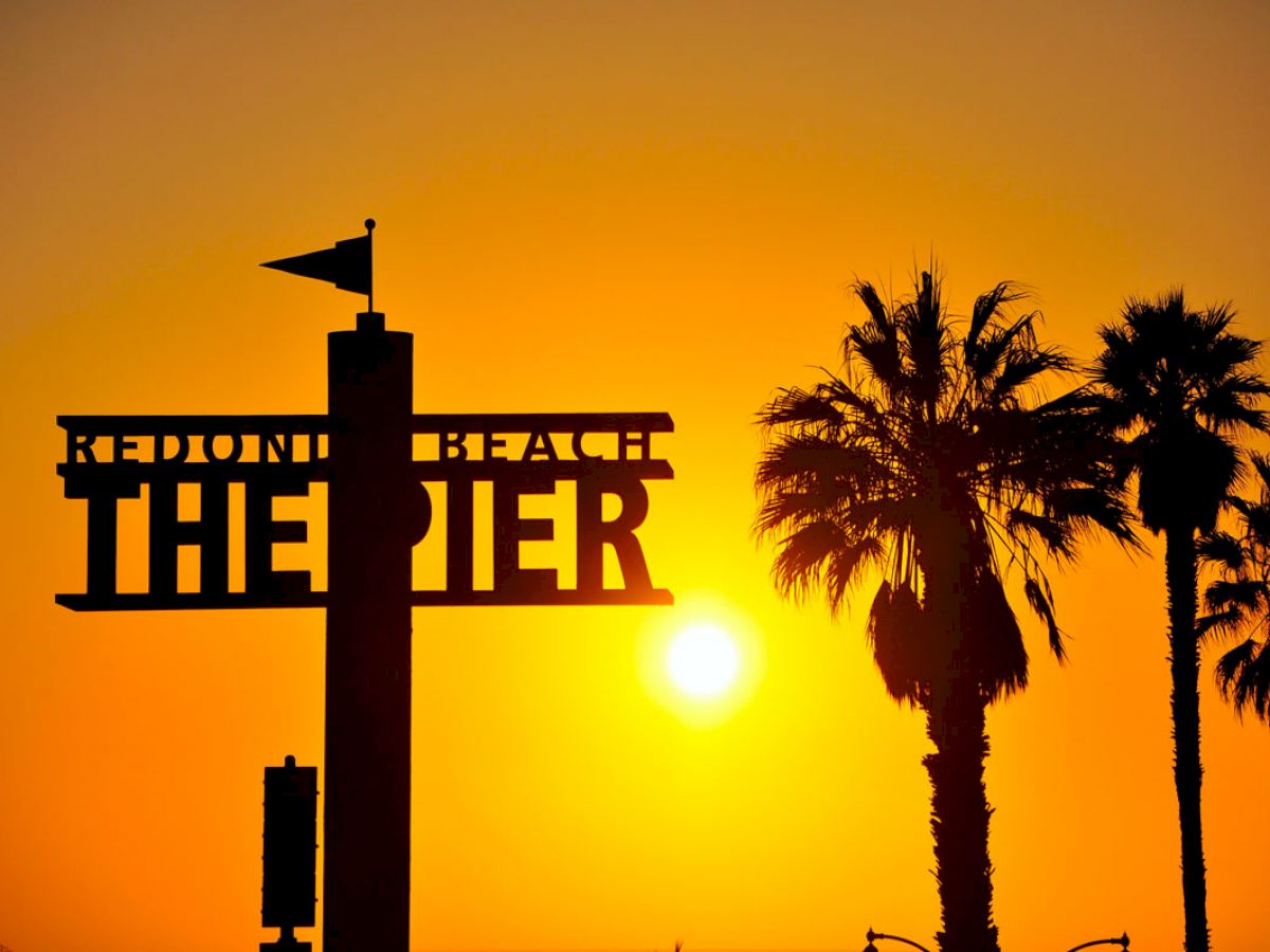 The image shows a sunset at Redondo Beach Pier, with a silhouette of palm trees and a sign reading 