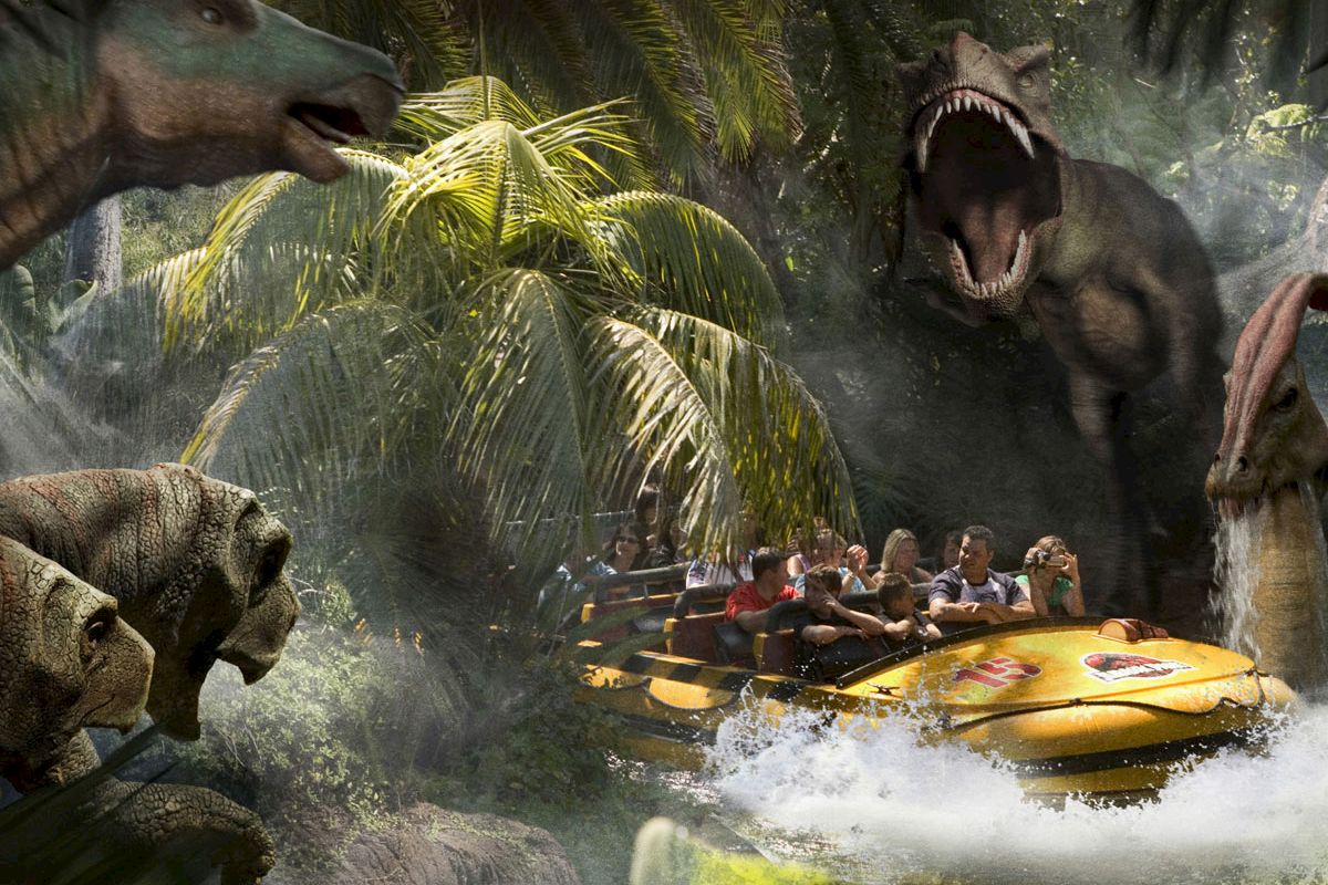 A group of people is on a water ride with large dinosaur models in a jungle setting, surrounded by splashing water and lush greenery.