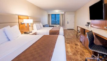 A modern hotel room with two double beds, a desk, a chair, a TV, and a window.